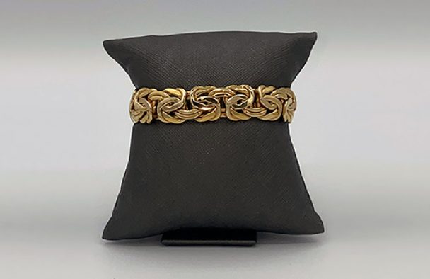 A bracelet on display wrapped around a black pillow with a grey background.